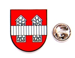 Wappen mit rotem Schild, weißen Häusern und blauem Streifen, daneben ein rundes Metallabzeichen mit Schrift.