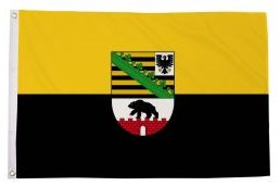 Gelbe, schwarze und weiße Flagge mit Wappen in der Mitte, darunter ein grünes Diagonalband.