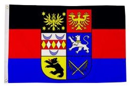 Flagge mit schwarzem, rotem und blauem Hintergrund sowie Wappen mit Adler, Löwen und Löwenkopf.